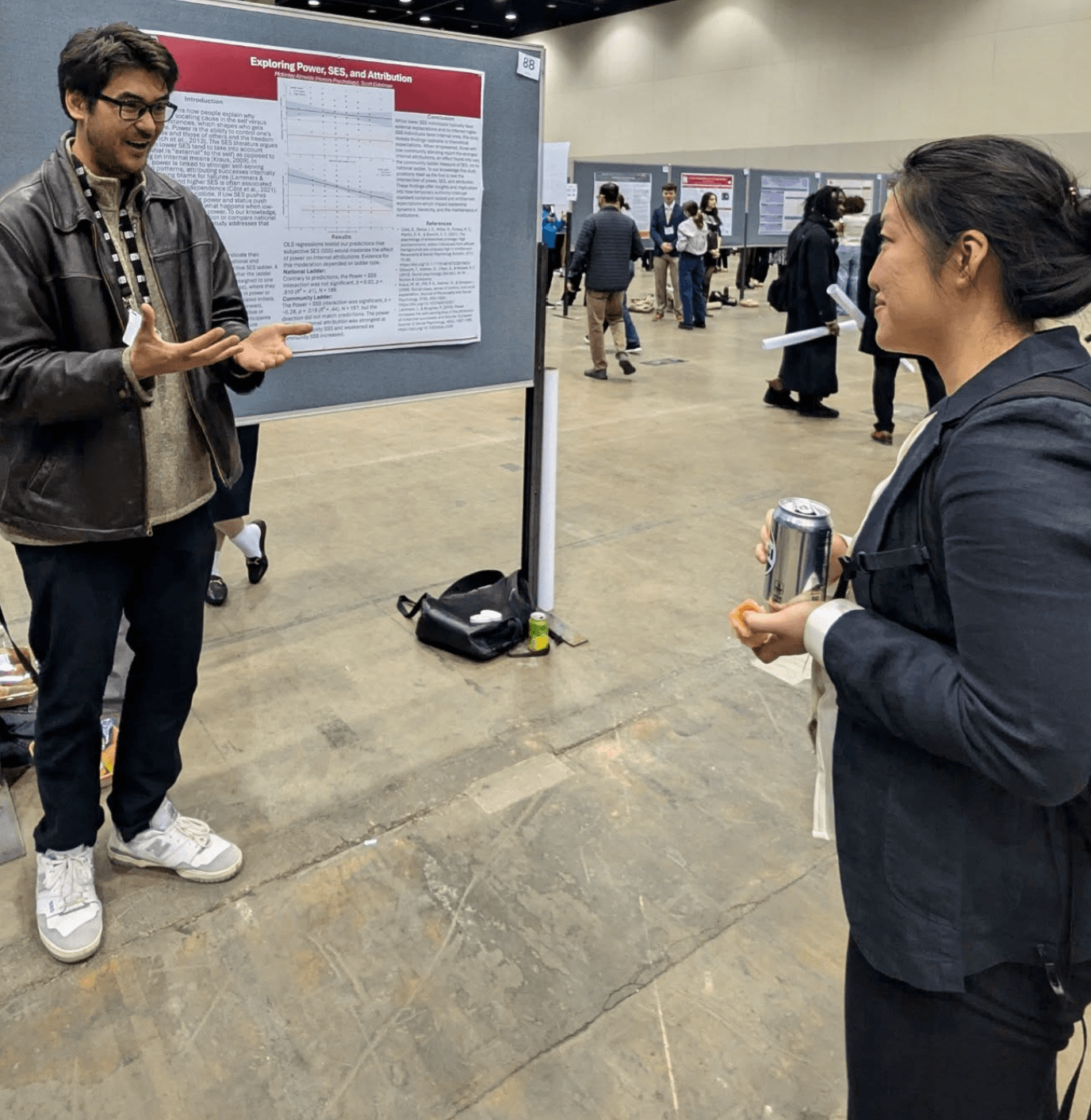 Mckinley Almeida discussing his Exploring Power, SES, and Attribution poster with an attendee at a research conference